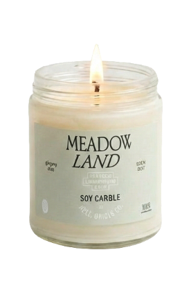 A lit candle in a clear glass jar with a cream-colored wax and a white label reading &