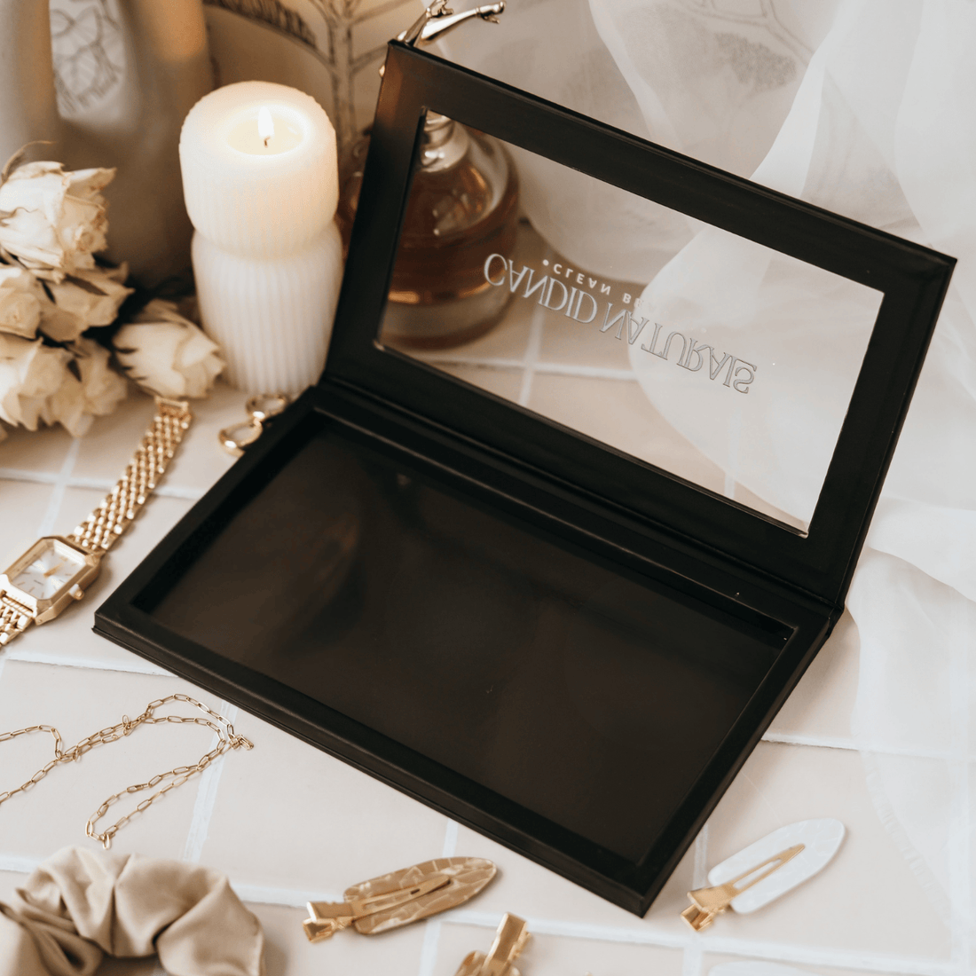 Open black jewelry box with a candle, flowers, and perfume bottle in the background
