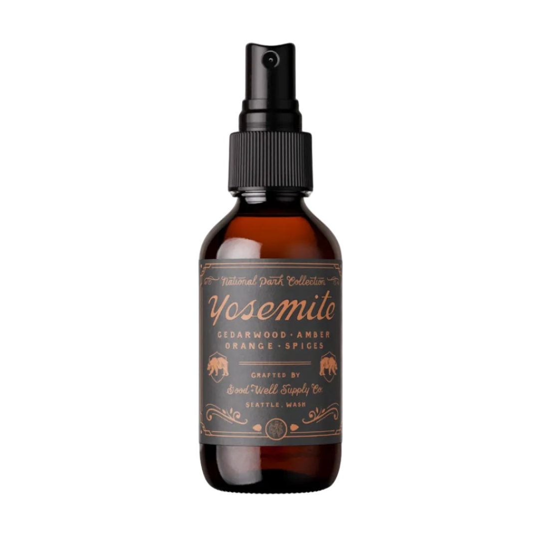 An amber glass spray bottle with a black spray top and a brown label reading Yosemite Cedarwood, Amber, Orange, Spices, on a plain white background.