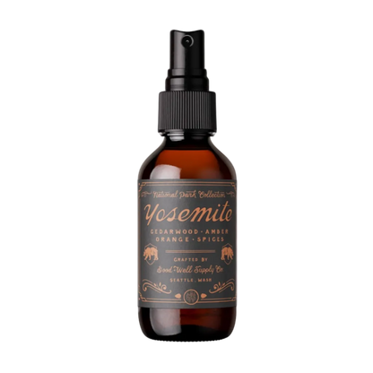 An amber glass spray bottle with a black spray top and a brown label reading Yosemite Cedarwood, Amber, Orange, Spices, on a plain white background.
