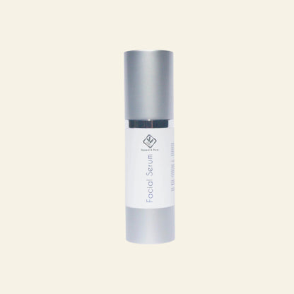 Facial serum bottle with silver cap and white body on a light gray background