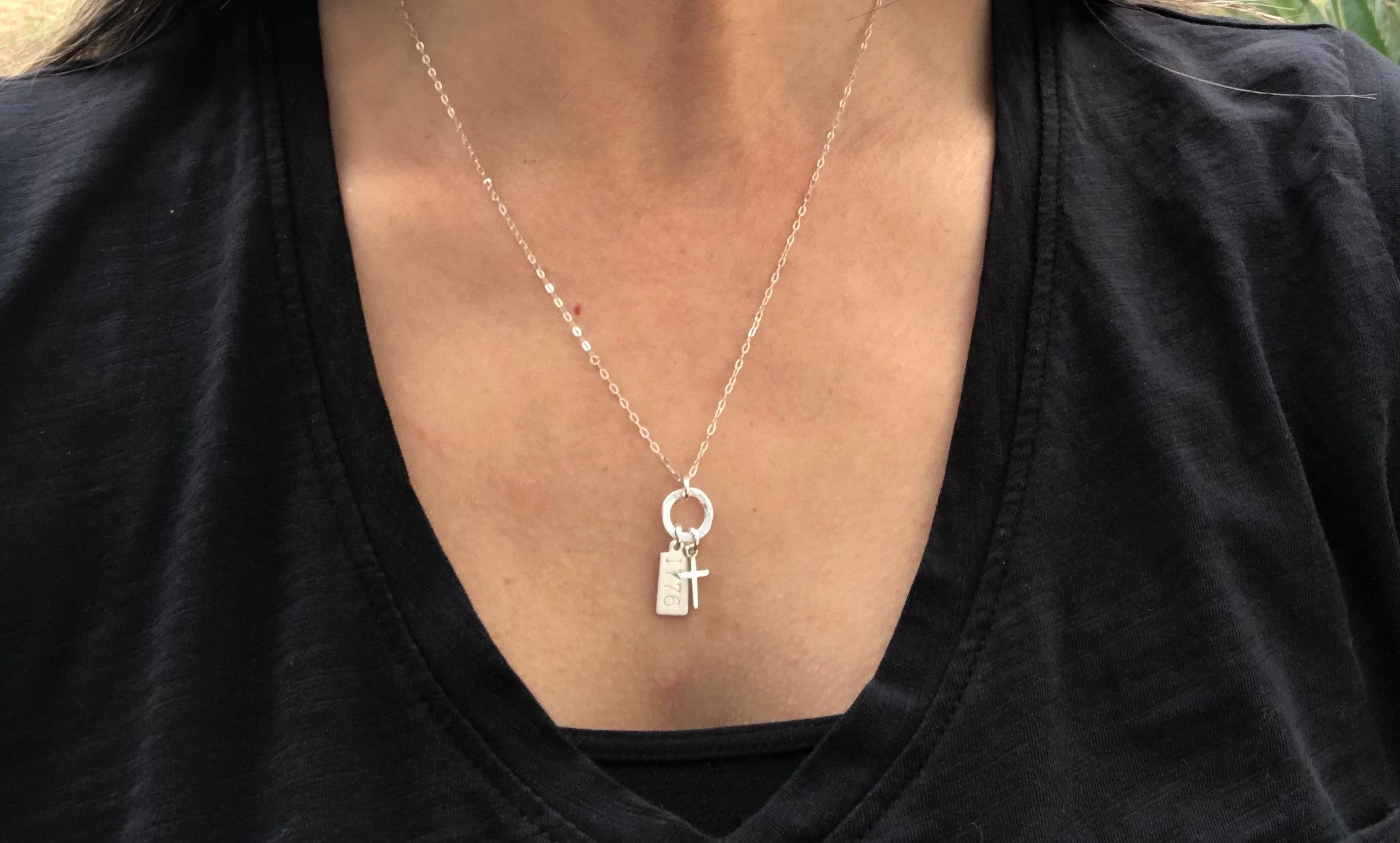 Silver necklace with a cross pendant worn by a person in a black shirt.