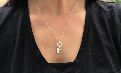 Silver necklace with a cross pendant worn by a person in a black shirt.