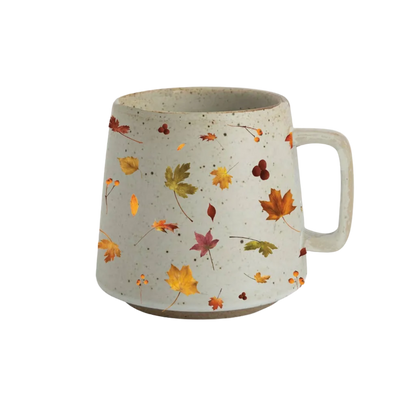 A speckled off-white ceramic mug with a handle, decorated with a pattern of colorful autumn leaves in orange, yellow, green, and red.