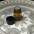 Small amber glass bottle with a black cap on a decorative white plate with black patterns