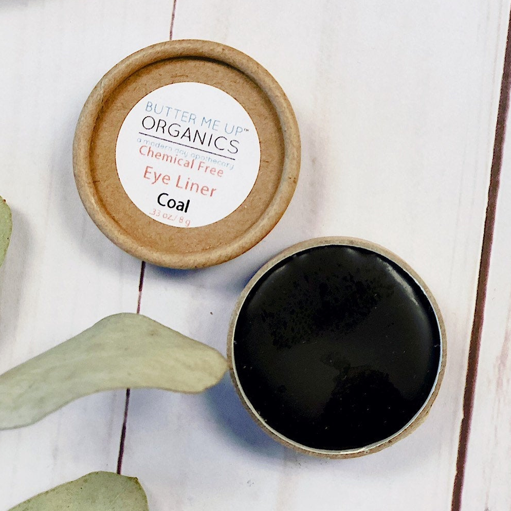 Cosmetic container with black liner and wooden lid on a light wooden surface with eucalyptus leaves.