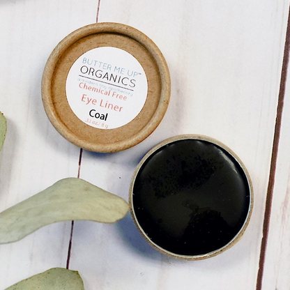 Cosmetic container with black liner and wooden lid on a light wooden surface with eucalyptus leaves.
