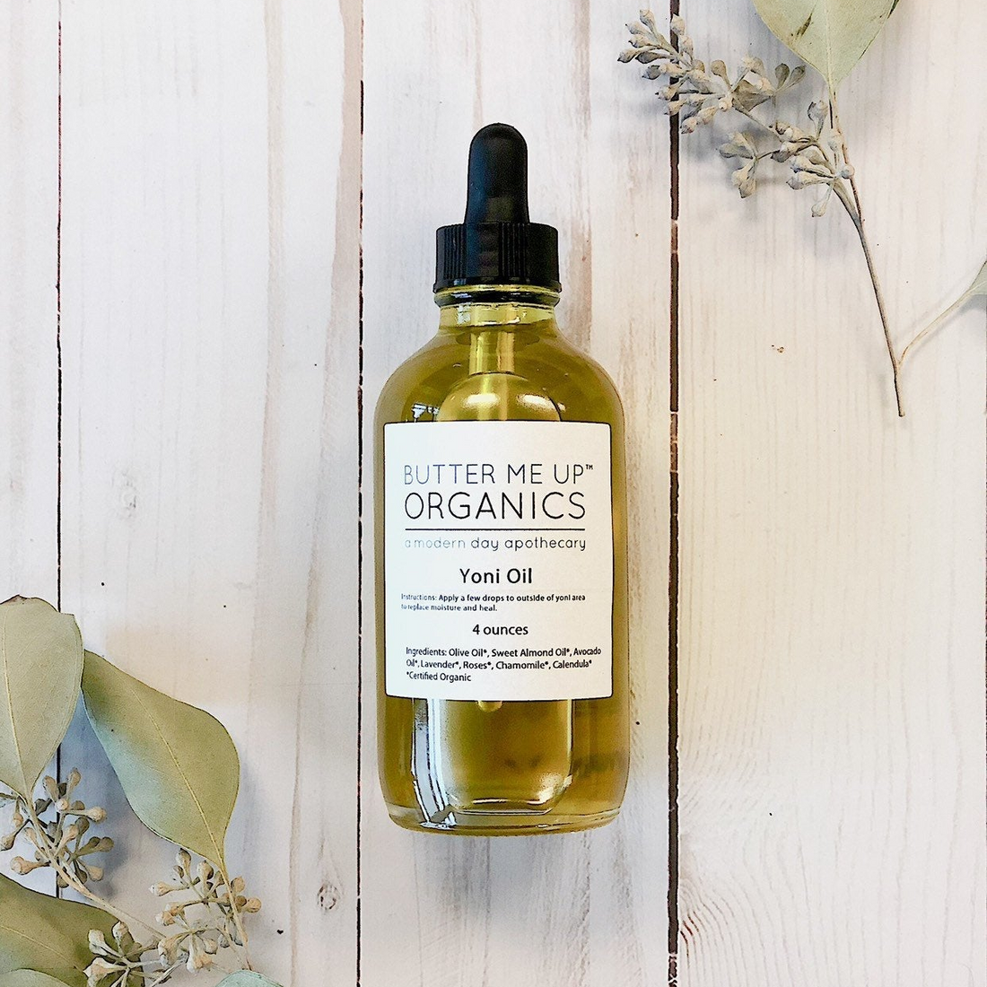 Butter Me Up Organics Yoni Oil bottle with dropper on a wooden surface with leaves.