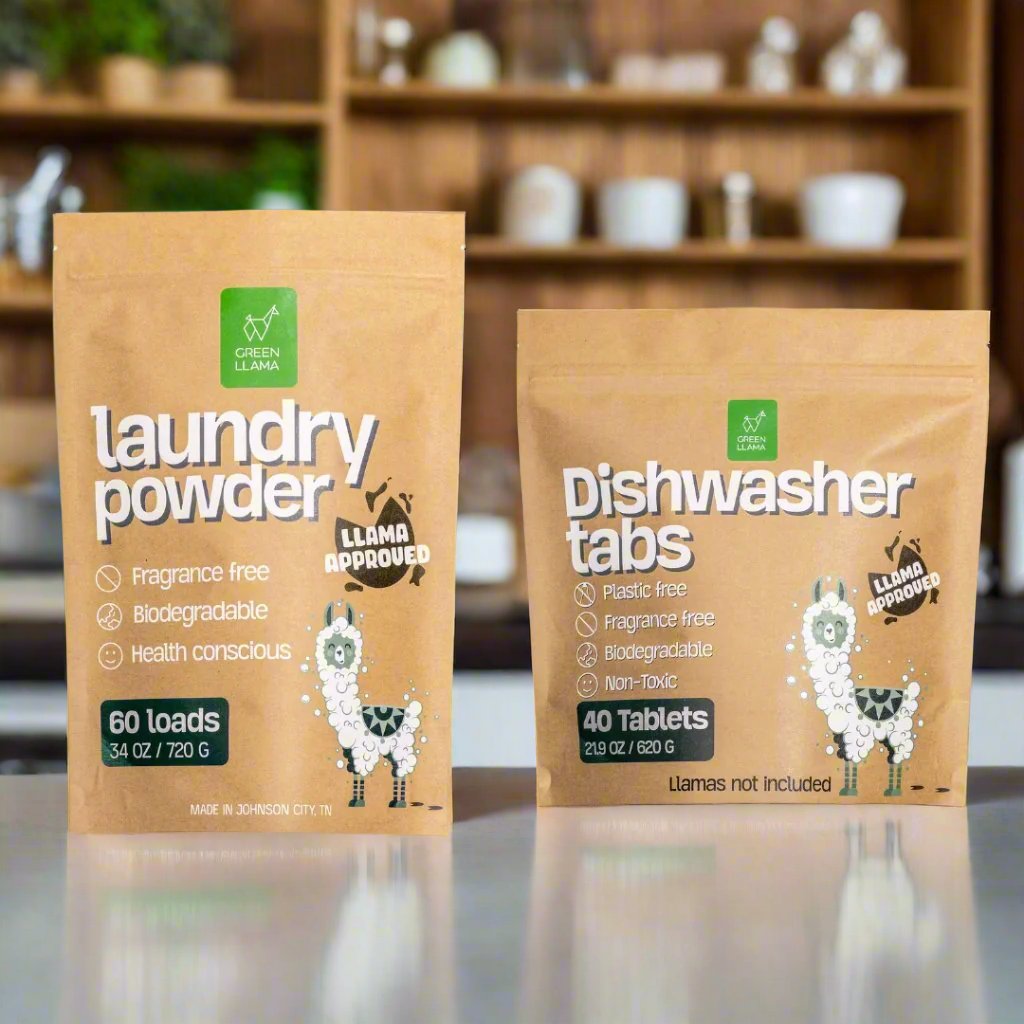 Two packages of laundry powder and dishwasher tabs with a llama-themed label on a reflective surface.
