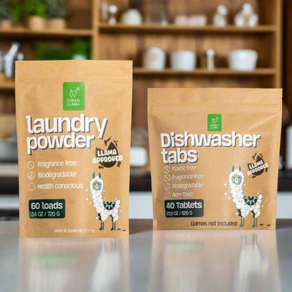 Two packages of laundry powder and dishwasher tabs with a llama-themed label on a reflective surface.