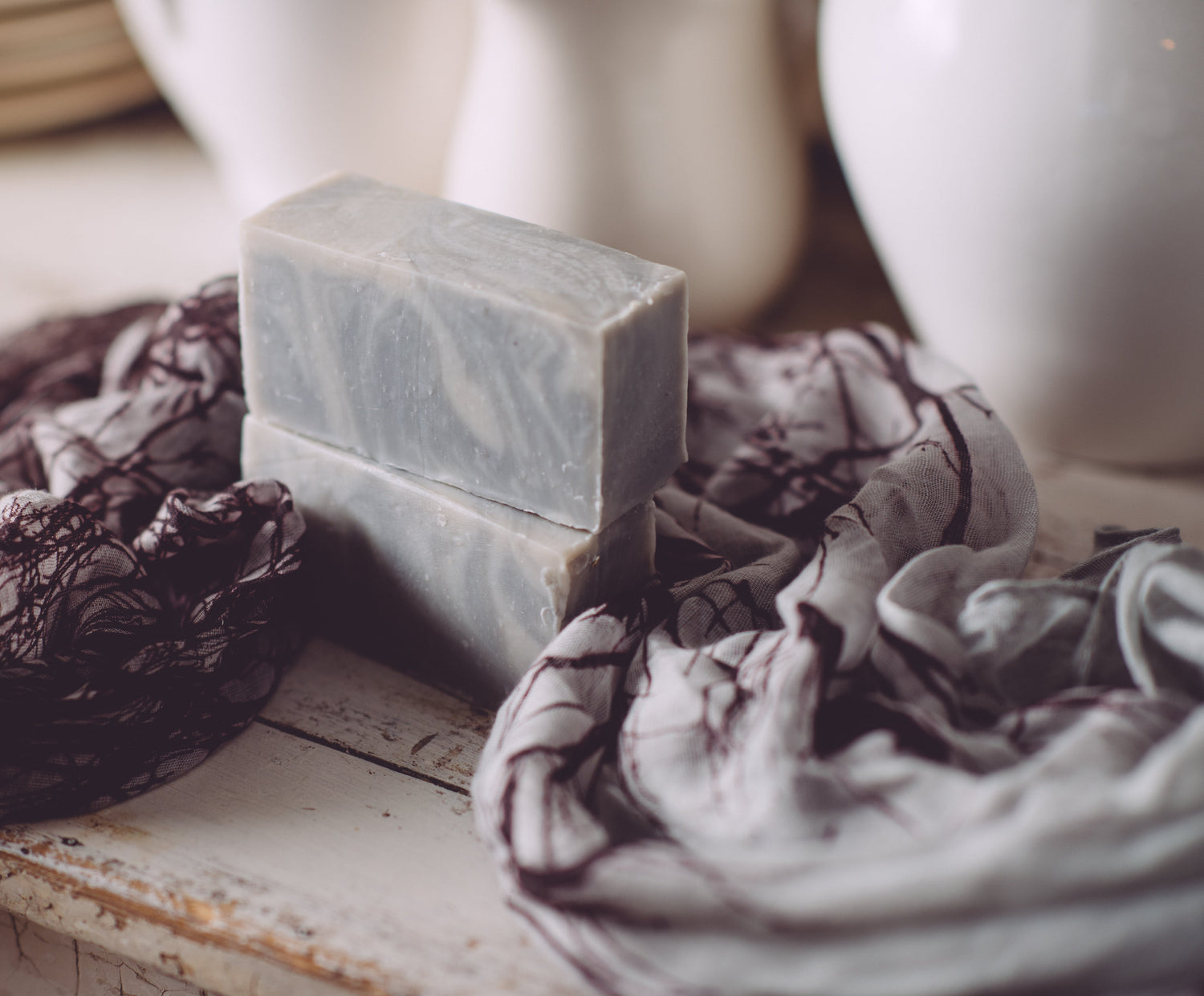 Two bars of soap on a textured surface with a cloth and blurred background