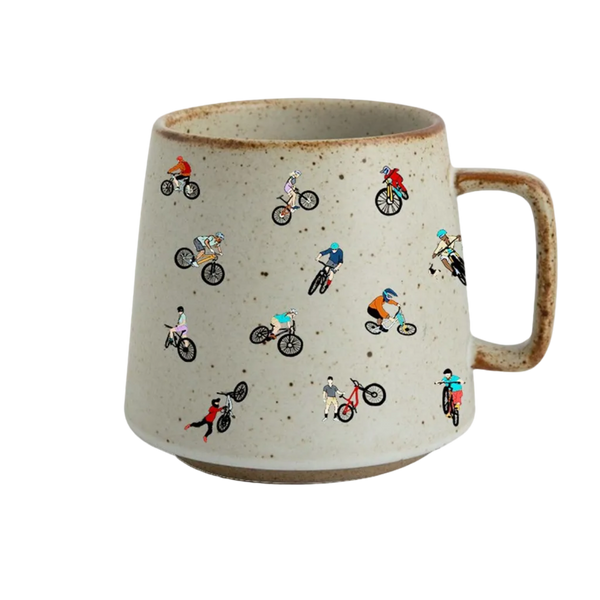 A speckled beige ceramic mug with a brown handle and rim, decorated with a playful pattern of small cartoon mountain bikers in various colorful outfits.