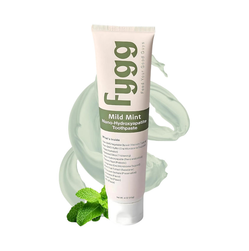 A tube of Fygg Mild Mint nano-hydroxyapatite toothpaste, featuring a pale pink and white design with green text, set against a white background with mint leaves and a mint-green toothpaste swirl graphic.