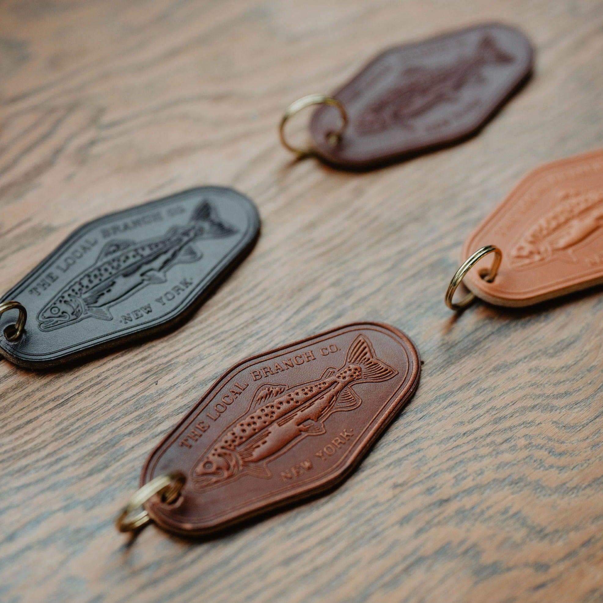 Three leather keychains with fish embossing on a wooden surface