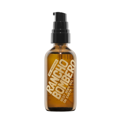 An amber glass pump bottle of Rancho Bombero Best Body Oil with a black pump dispenser and gold lettering, isolated on a white background.