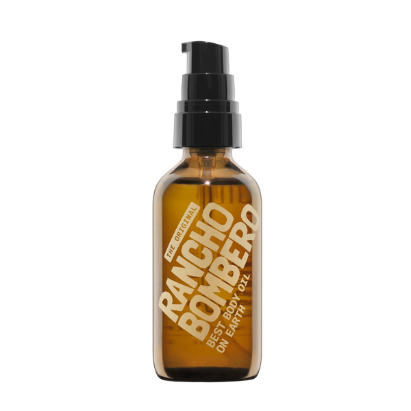 An amber glass pump bottle of Rancho Bombero Best Body Oil with a black pump dispenser and gold lettering, isolated on a white background.