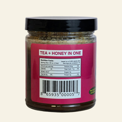 A jar of tea and honey product with a black lid and a bright pink label showing nutrition facts and a barcode, photographed against a light neutral background.