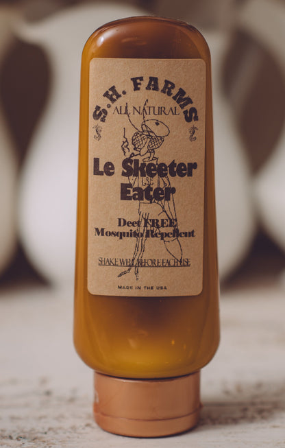 Bottle of S. H. Farms Le Skeeter Eater on a wooden surface with blurred background