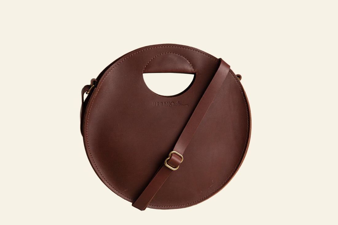 Brown circular handbag with a strap on a white background
