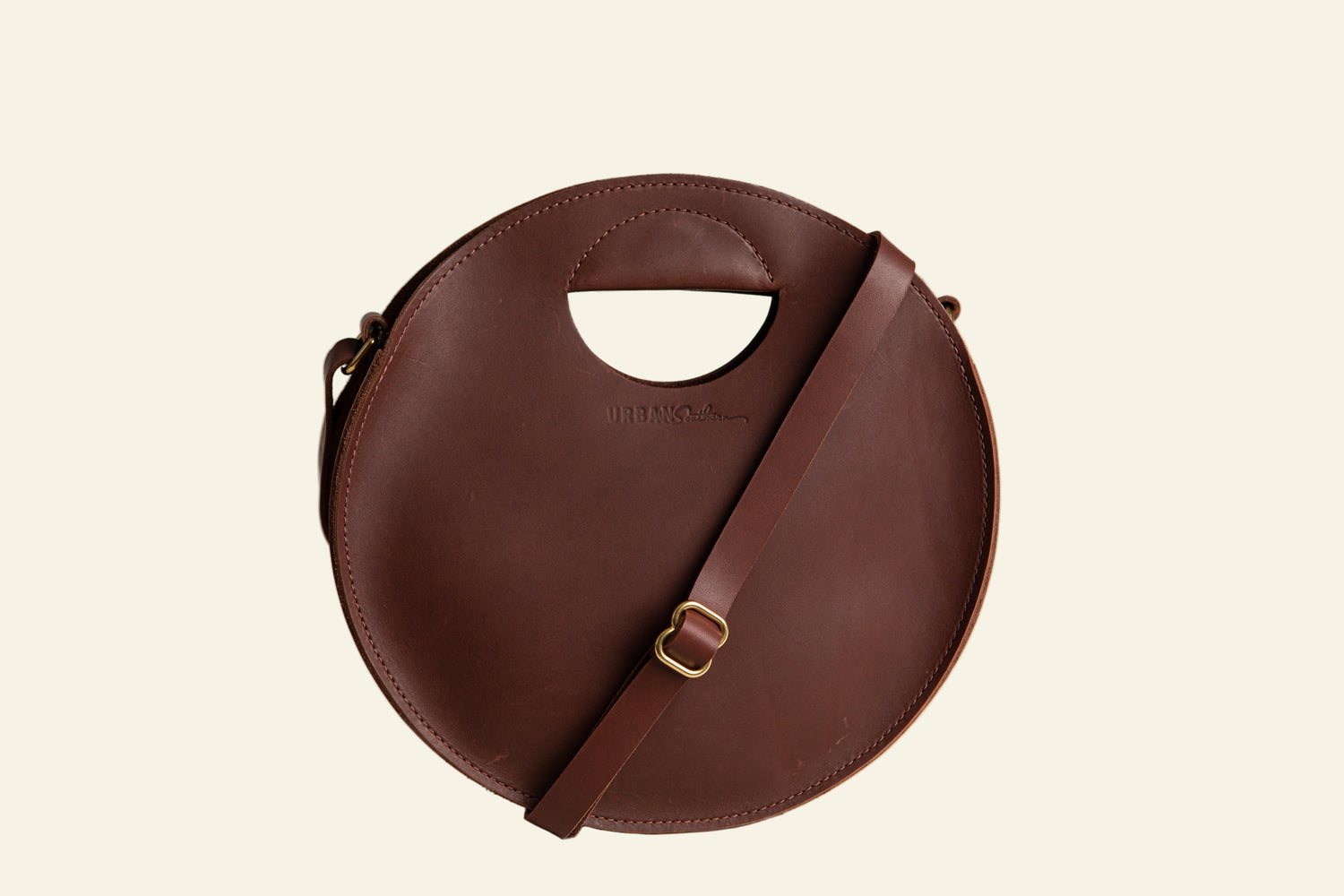 Brown circular handbag with a strap on a white background