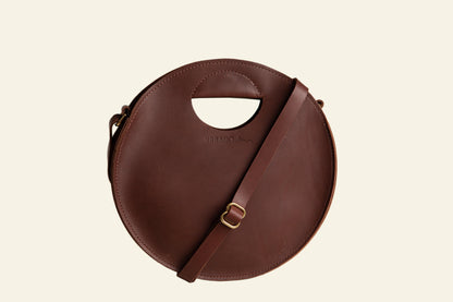 Brown circular handbag with a strap on a white background
