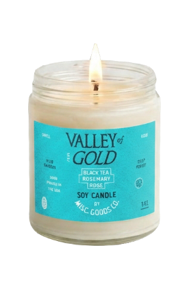 A lit soy candle in a clear glass jar with a turquoise label reading &