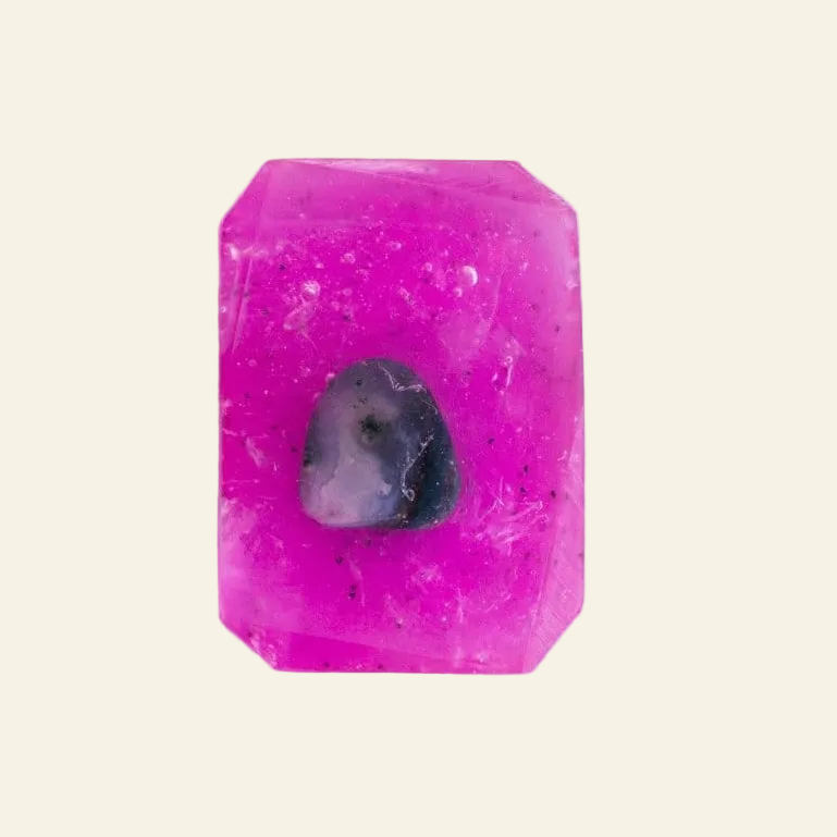A bright pink rectangular gemstone with a small dark purple inlay in the center, displayed on a light gray marble surface.