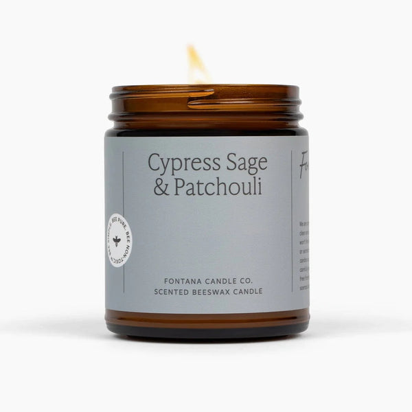 A lit amber glass jar candle with a gray label reading 'Cypress Sage & Patchouli' and 'Fontana Candle Co.' on a clean white background.