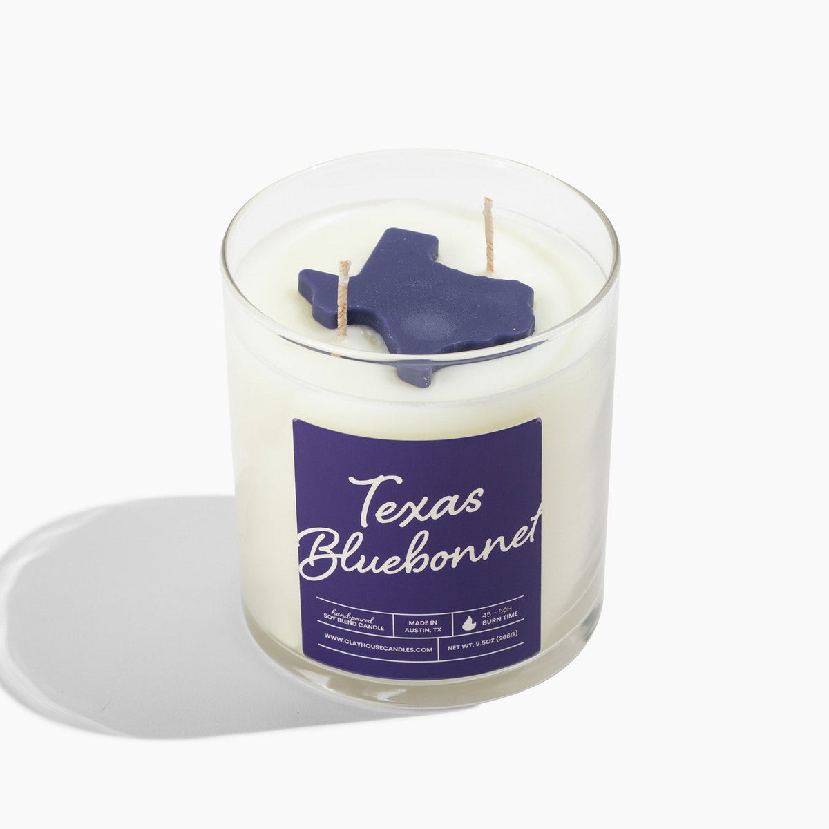 A white soy wax candle in a clear glass jar with a purple label reading &