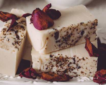 Three pieces of white soap with dark specks, garnished with dried red flowers on a white surface.